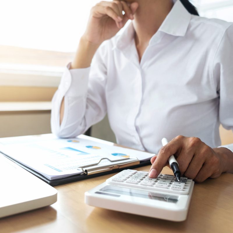 Female accountant calculations and analyzing financial graph data with calculator and laptop Business, Financing, Accounting, Doing finance, Economy, Savings Banking Concept.